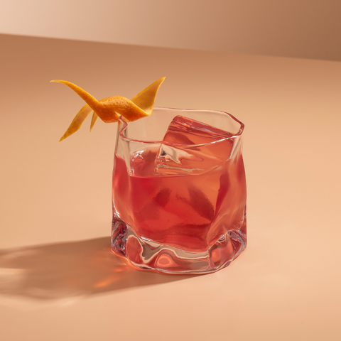 Pink cocktail in a glass with an orange twist on a beige background